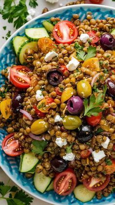 a blue and white plate filled with lentils, tomatoes, cucumbers, olives, feta cheese and parsley