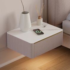 a white table with a cell phone on it next to a vase and reeds