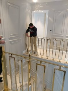 a man standing on top of a stair case in a room with white walls and gold railings