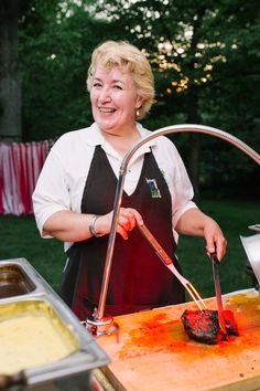 a woman in an apron cooking food on a grill with tongs and spatula