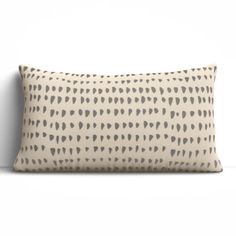 a beige and black pillow with hearts on it, sitting against a white wall in the corner