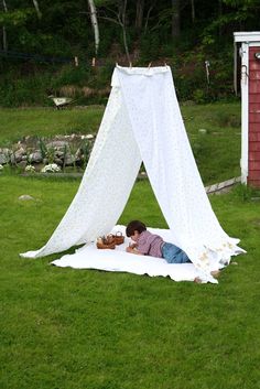 a little boy laying on top of a blanket in the grass next to a tent