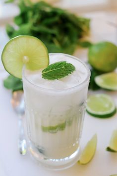 a glass filled with ice and limes on top of a white table next to sliced limes