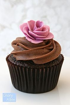 a cupcake with chocolate frosting and a pink flower on top is sitting on a white surface