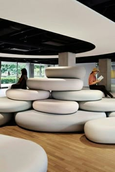 a woman sitting on top of a stack of white round chairs in a room filled with windows