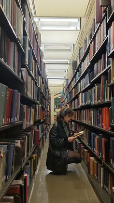 a woman is sitting on the floor reading a book in a library full of books