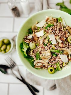 a green bowl filled with food next to silverware on a white tiled counter top