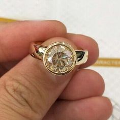 a person holding a ring with a diamond in it's middle and gold band