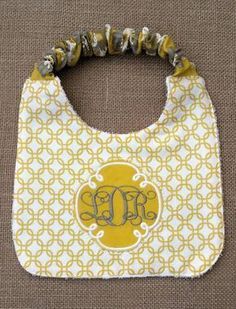 a yellow and white bib with the monogrammed initials on it, sitting on a brown background