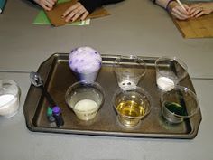 three people are sitting at a table working on an art project with colored liquid and paper