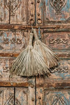 an old door with two straw brooms hanging from it's handle, and ornate carvings on the doors