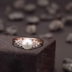 a pearl and diamond ring sitting on top of a wooden block with rocks in the background