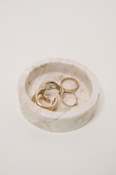 two pairs of gold rings sitting on top of a white marble bowl with one ring in the middle