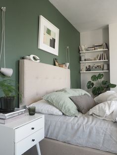 a bedroom with green walls, white bedding and plants on the nightstand next to it