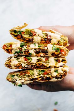 a hand holding three tacos filled with meat, cheese and vegtables