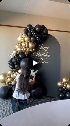 a woman standing in front of a black and gold balloon arch