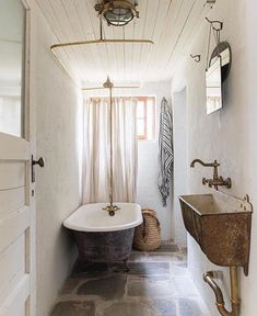 an old fashioned bathtub and sink in a bathroom with white walls, stone flooring and