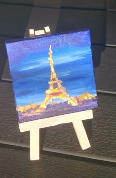 a small easel with a painting of the eiffel tower on it's side