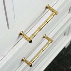 two gold handles on the side of a white cabinet