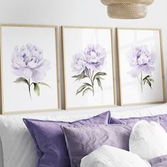 three purple flowers are hanging on the wall above a bed with white sheets and pillows