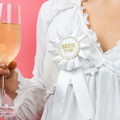 a woman holding a glass of wine in her right hand and a white ribbon around her neck