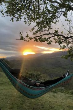 a person laying in a hammock with the sun setting