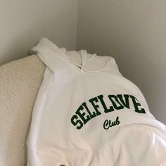 a white sweatshirt with the words self love club on it sitting on a couch in a corner