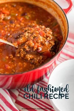 a red pot filled with chili next to a white and red striped napkin on top of a table