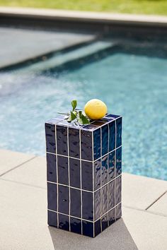 a blue vase sitting on top of a tiled floor next to a swimming pool with a lemon in it