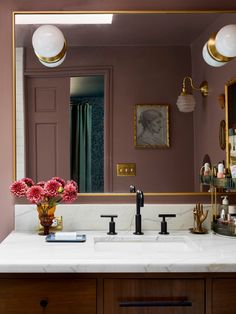 a bathroom vanity with marble counter top and gold framed mirror above it, along with pink flowers