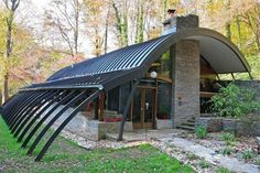 an unusual house in the woods with its roof made out of solar panels and metal tubes