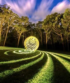 a large yellow ball sitting in the middle of a lush green field next to trees