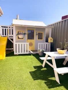 a small yellow and white shed with picnic table next to it on the grass in front of a building