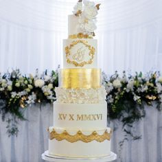 a three tiered wedding cake with white and gold decorations on the top, surrounded by flowers