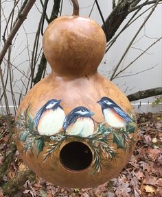 a birdhouse with three birds painted on it's sides and leaves around the base