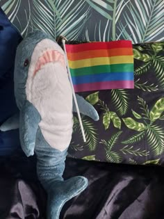 a stuffed shark with a rainbow flag sticking out of it's mouth sitting on a bed