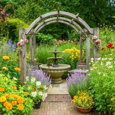 a garden filled with lots of flowers next to a wooden arbor covered in plants and water fountain