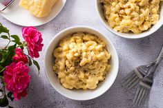 three bowls filled with macaroni and cheese on top of a table next to flowers