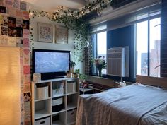 a bedroom with a bed, television and window in the room that has plants growing on the wall