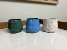 three small cups sitting on top of a white table next to each other, one blue and one green