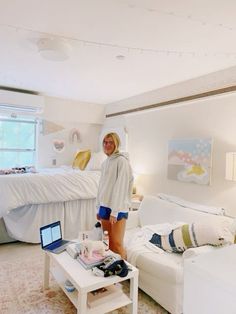 a woman standing next to a bed in a room with white furniture and decor on the walls