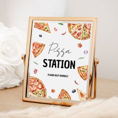 a pizza station sign sitting on top of a wooden table next to a white flower