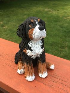 a dog figurine sitting on top of a wooden bench in front of some grass