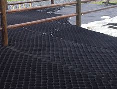 a sheep standing on top of a black tarp next to a wooden fence