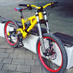 a yellow bicycle parked on top of a wooden bench next to a brick wall with red rims