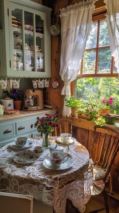 a table with plates and cups on it in front of a window filled with potted plants