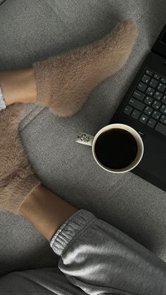 a person's feet on a couch next to a coffee cup and laptop computer