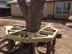 a tree that is sitting in the dirt near a house with a wooden frame around it