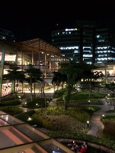 a night time view of a building with lots of plants and trees in the foreground