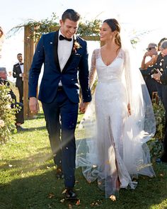 a man and woman are walking through the grass together in front of people wearing tuxedos